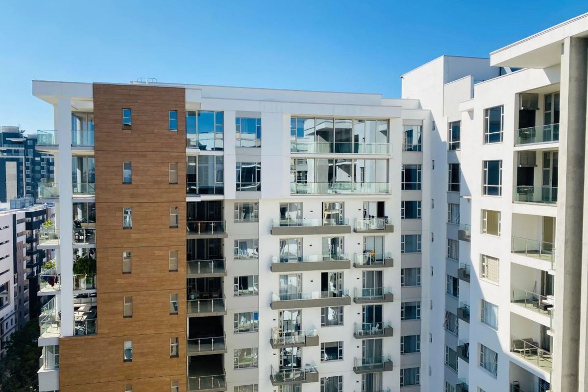 A modern apartment building exterior featuring clean white facades, wood-look cladding accents, and multiple private balconies with glass railings.