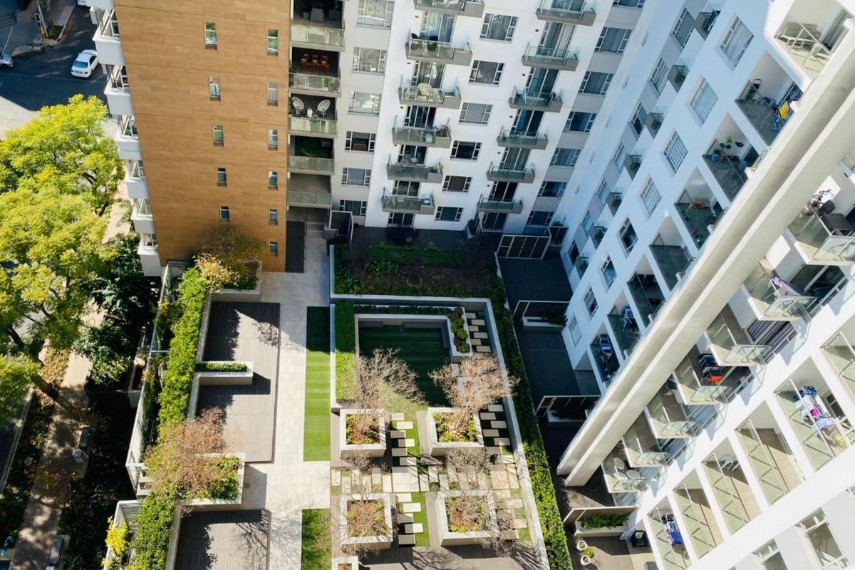 An aerial view of the apartment complex featuring a well-maintained central courtyard with landscaped gardens, paved pathways, and multiple residential balconies.