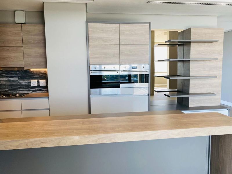 Modern kitchen featuring wood-finish cabinetry, built-in double ovens, a stone backsplash, and a central island with a breakfast bar.