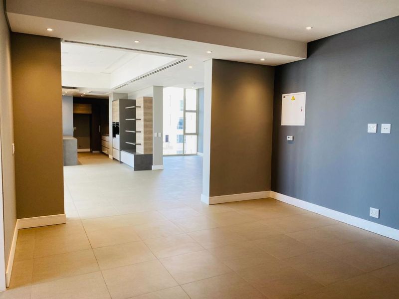 Spacious open-plan living area featuring neutral tiled flooring, recessed lighting, and a modern kitchen layout with built-in cabinetry and large windows.