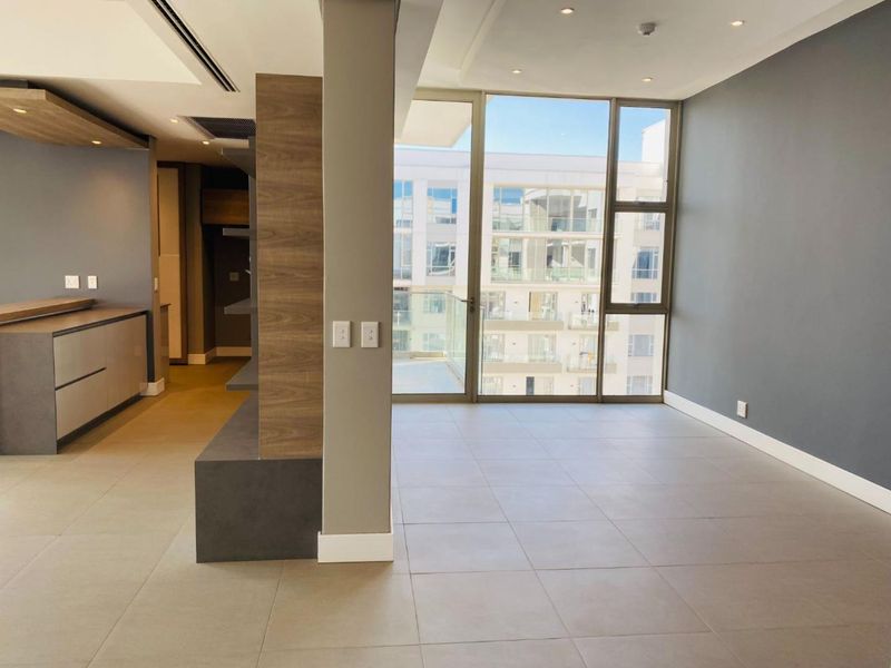 Modern open-plan living area featuring large floor-to-ceiling windows, neutral tiled flooring, recessed lighting, and sleek built-in cabinetry with a contemporary finish.