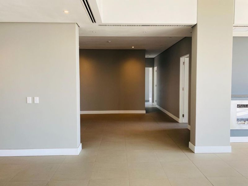 A spacious, empty living area featuring neutral tiled floors, recessed lighting, and a modern built-in fireplace, offering a clean and versatile blank canvas.