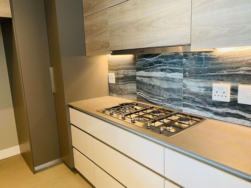 Modern kitchen featuring a gas hob, integrated extractor fan, stone splashback, and sleek built-in cabinetry with under-cabinet lighting.