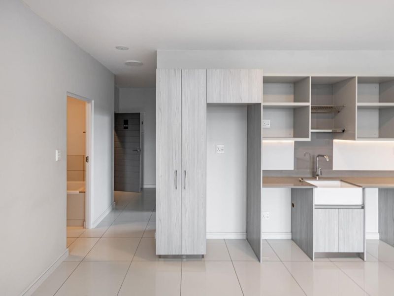 Modern kitchen area featuring light wood-grain cabinetry, integrated shelving, and a clean undermount sink, set within a bright, tiled open-plan space.