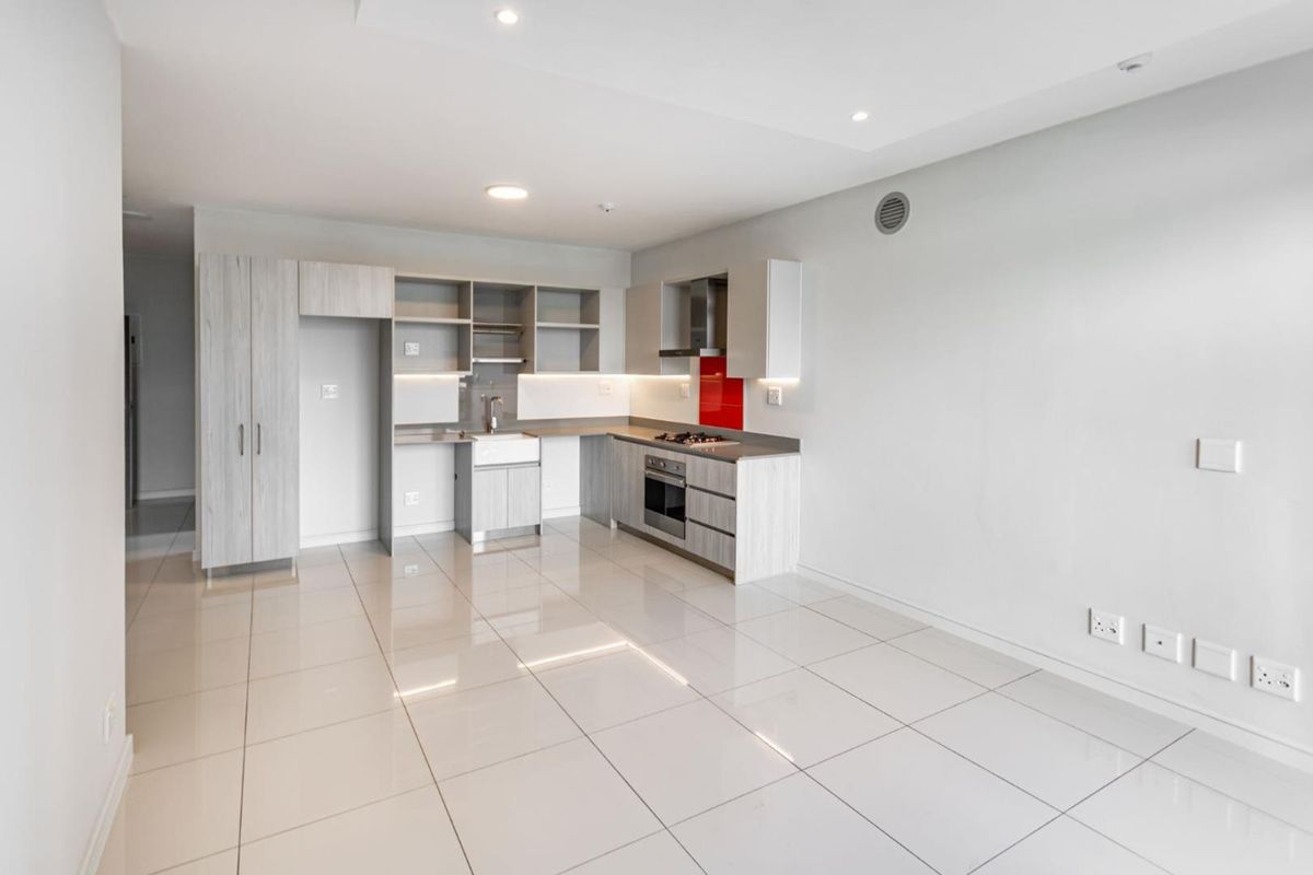 Modern open-plan kitchen featuring light wood-grain cabinetry, a red glass splashback, integrated gas hob, electric oven, and sleek ceramic floor tiles.