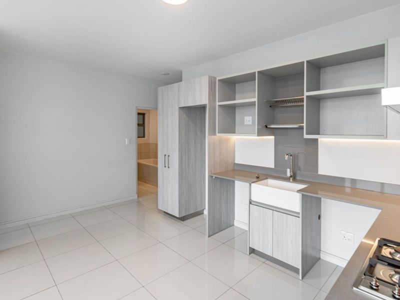 Modern kitchen featuring light wood-grain cabinetry, a farmhouse sink, gas hob, and sleek tiled flooring with integrated under-cabinet lighting.
