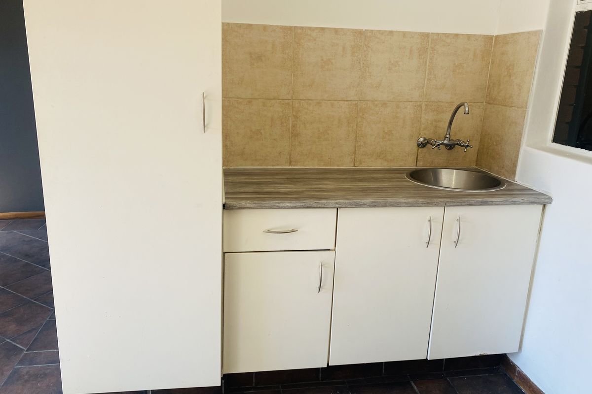 A compact kitchen area featuring built-in white cabinetry, a laminate countertop, a stainless steel sink, and a tiled backsplash.