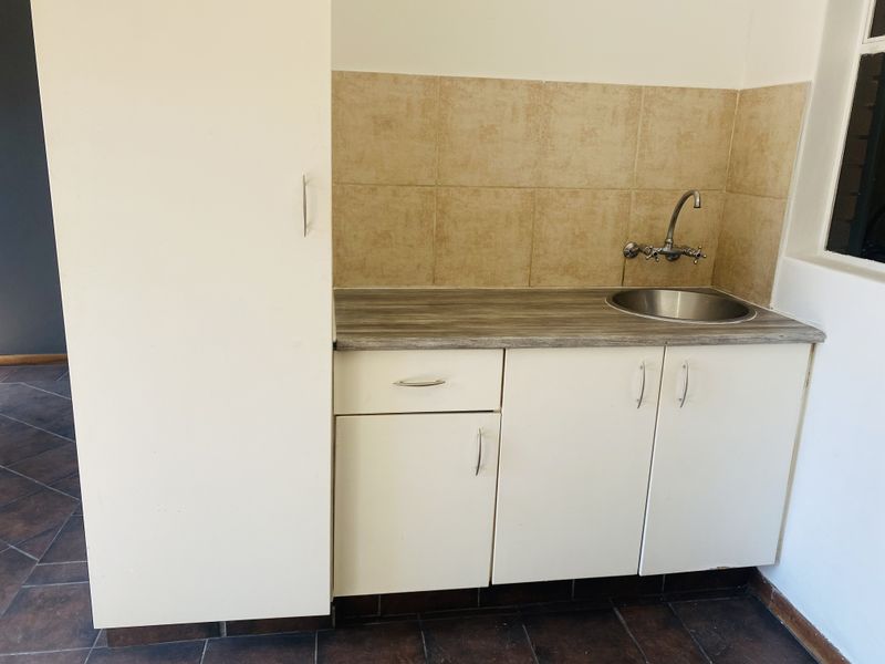 A compact kitchen area featuring built-in white cabinetry, a laminate countertop, a stainless steel sink, and a tiled backsplash.