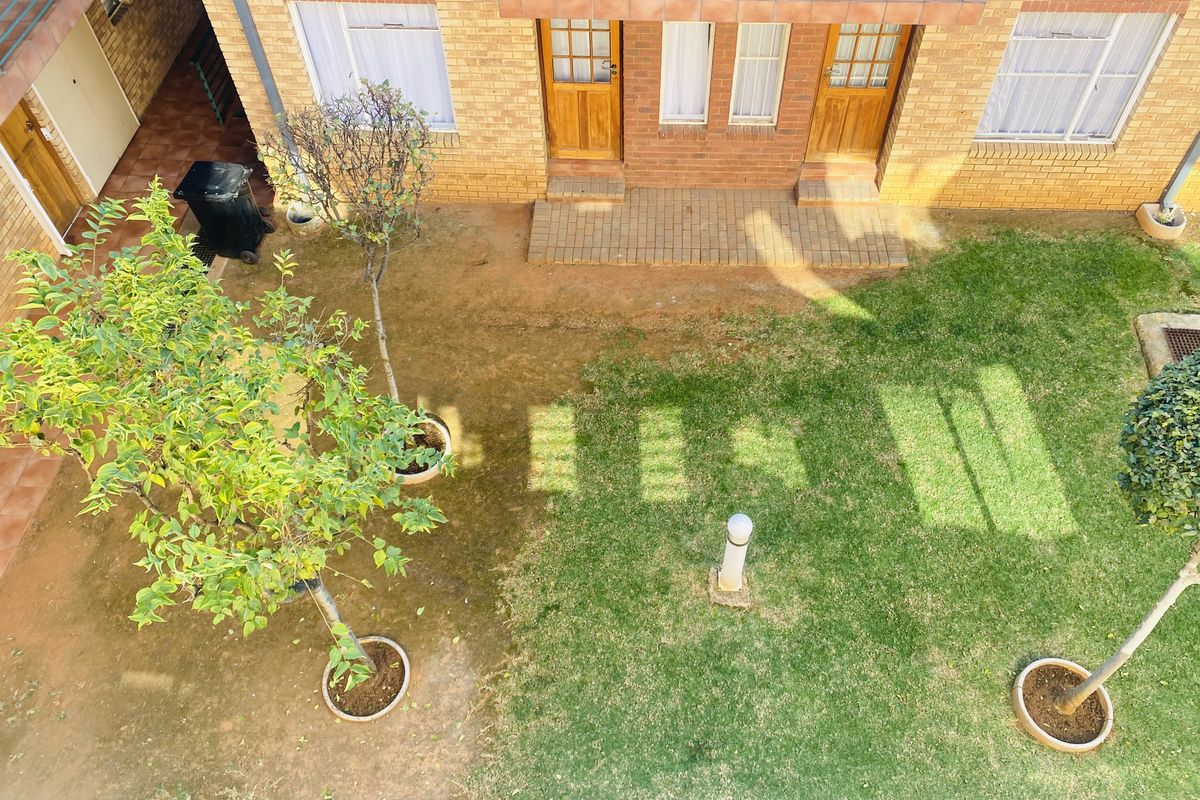An elevated view of a communal garden area featuring a brick apartment facade with timber entrance doors and a small paved walkway.