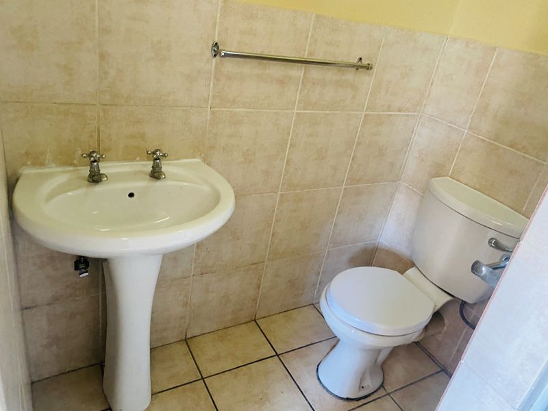 A functional bathroom featuring a pedestal basin, standard toilet, and neutral ceramic wall and floor tiling.