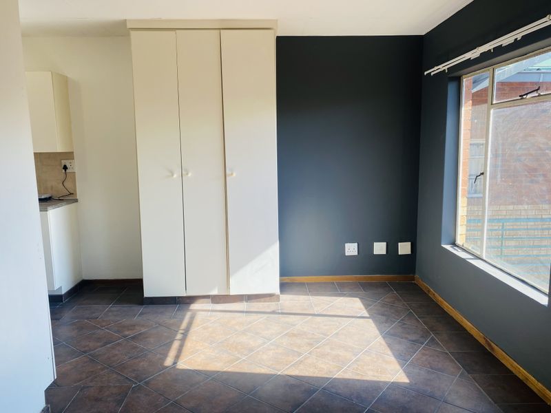 A bright, empty bedroom featuring tiled flooring, a built-in wardrobe, and a large window with natural light.