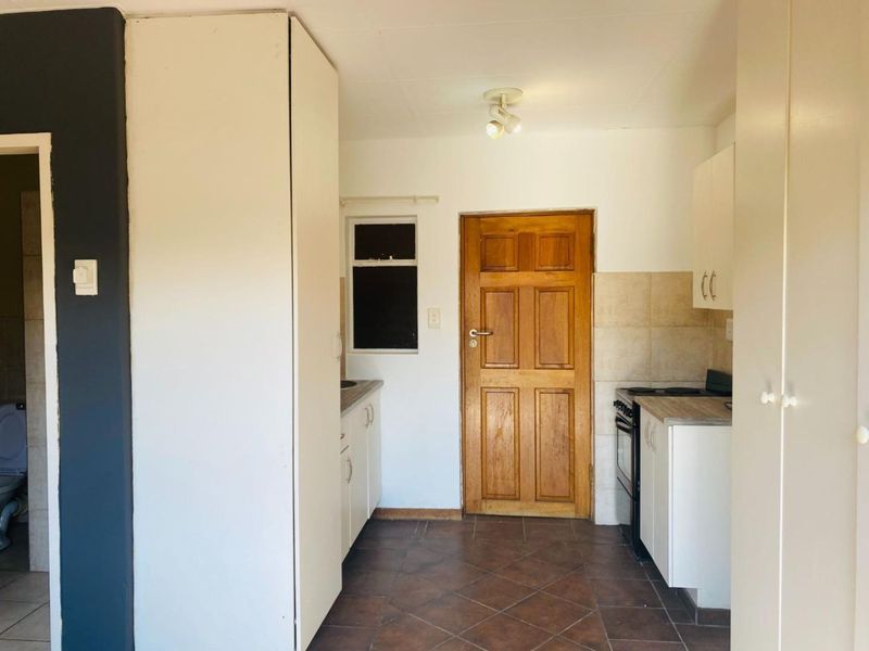 A functional kitchen featuring built-in cabinetry, tiled backsplash, and tiled flooring, with a direct view into an adjacent bathroom area.