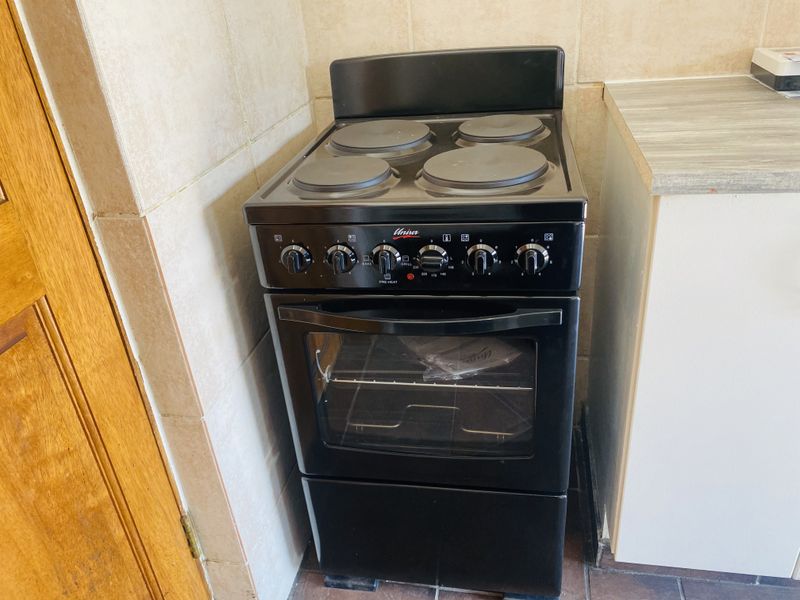 A clean kitchen corner featuring a black freestanding electric stove with a four-plate hob and oven, set against tiled splashbacks and a laminate countertop.