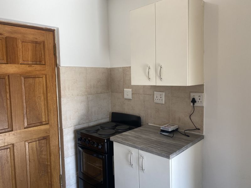 Compact kitchen area featuring built-in cabinetry, a laminate countertop, tiled splashback, and a freestanding stove.