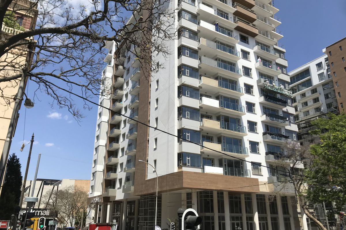 A modern high-rise apartment building featuring glass balconies, contemporary facade finishes, and ground-level commercial space in an urban setting.