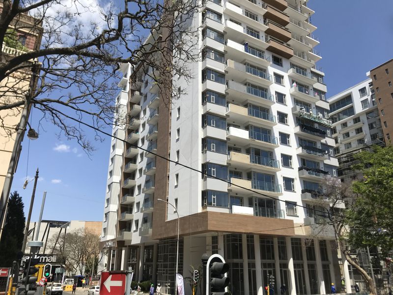A modern high-rise apartment building featuring glass balconies, contemporary facade finishes, and ground-level commercial space in an urban setting.