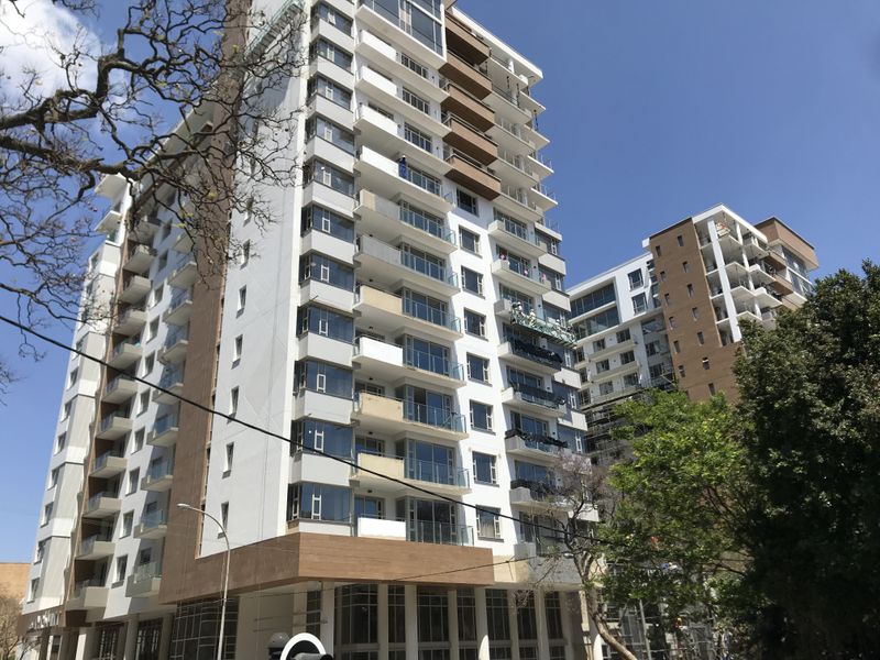 A modern multi-story apartment building featuring glass balconies and contemporary facade cladding under a clear blue sky.