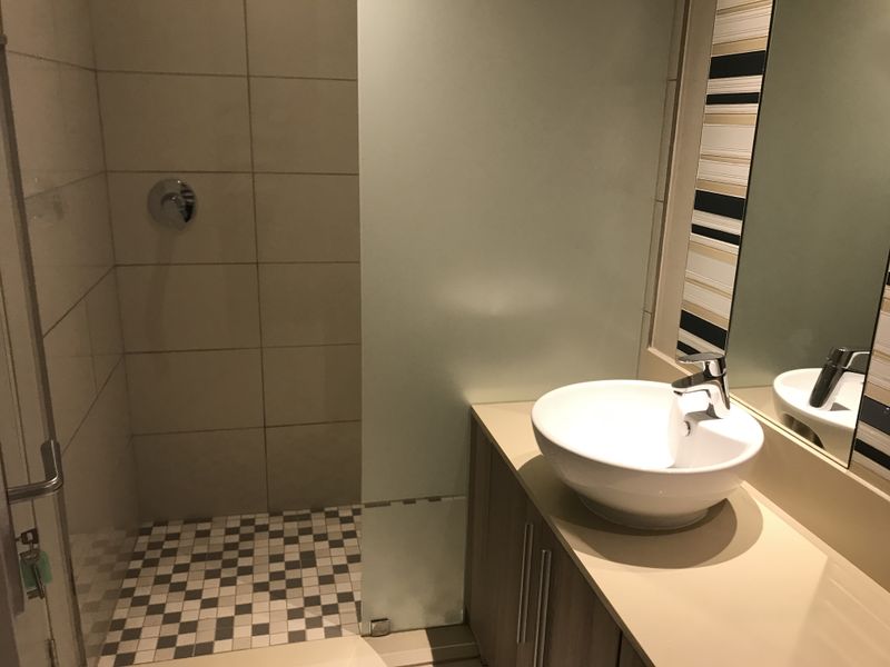 Modern bathroom featuring a vessel sink on a vanity cabinet, a tiled shower enclosure with a frosted glass partition, and contemporary wall finishes.