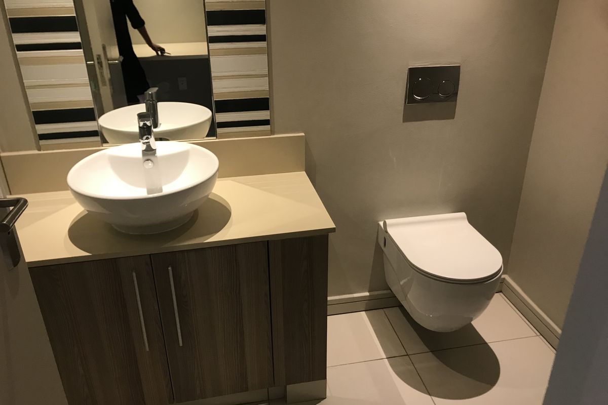 A modern bathroom featuring a wall-mounted toilet, a vanity cabinet with a vessel sink, and neutral tiled flooring.