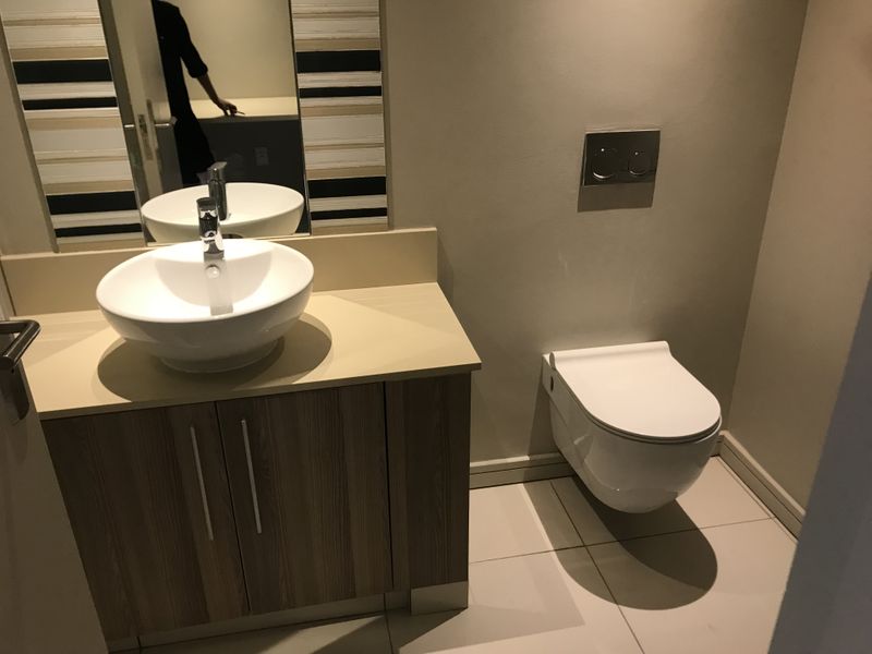 A modern bathroom featuring a wall-mounted toilet, a vanity cabinet with a vessel sink, and neutral tiled flooring.