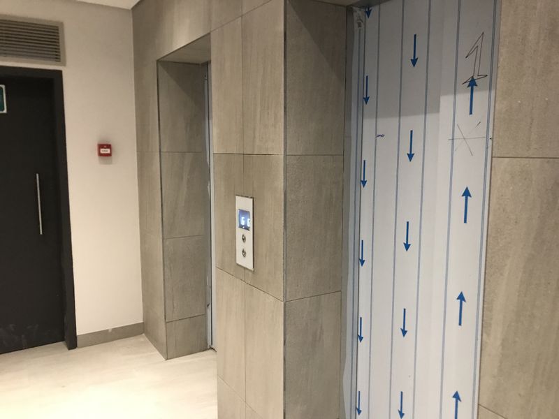 A modern apartment building hallway featuring tiled wall finishes and an elevator with protective construction film still attached.