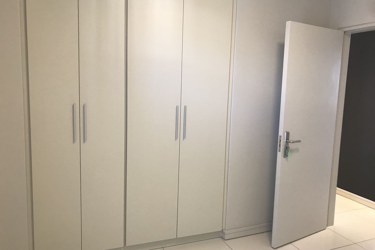 A clean, empty bedroom featuring neutral built-in cupboards, tiled flooring, and a simple interior door, offering a blank canvas for personalization.