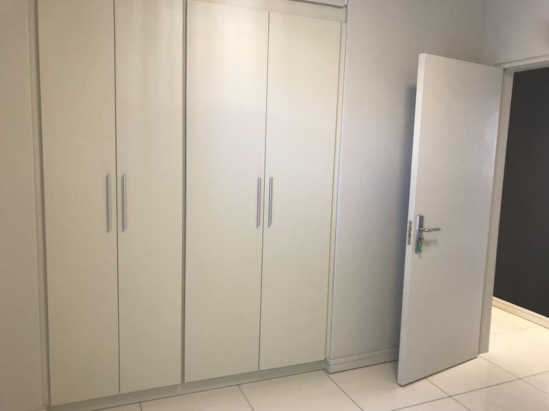 A clean, empty bedroom featuring neutral built-in cupboards, tiled flooring, and a simple interior door, offering a blank canvas for personalization.