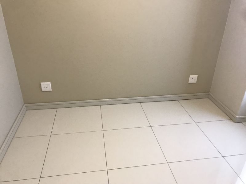 An empty interior space featuring neutral-toned walls, tiled flooring, and installed electrical sockets, providing a clean and versatile area.