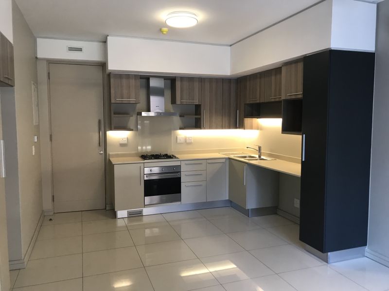 Modern kitchen featuring built-in cabinetry, gas hob, electric oven, extractor fan, and tiled flooring in a clean, contemporary layout.