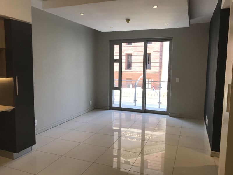 Modern open-plan living area featuring polished porcelain tiles, recessed ceiling lighting, and a sliding glass door leading to a private balcony.