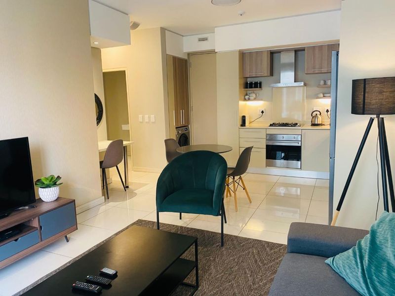 Modern open-plan living area featuring a compact kitchen with built-in appliances, sleek cabinetry, and polished tiled flooring throughout the space.