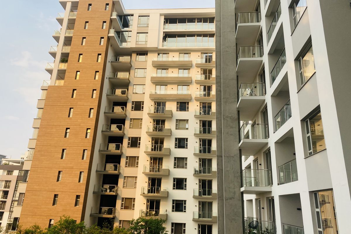 A modern high-rise apartment building exterior featuring multiple balconies with glass balustrades and a mix of textured cladding and painted concrete finishes.