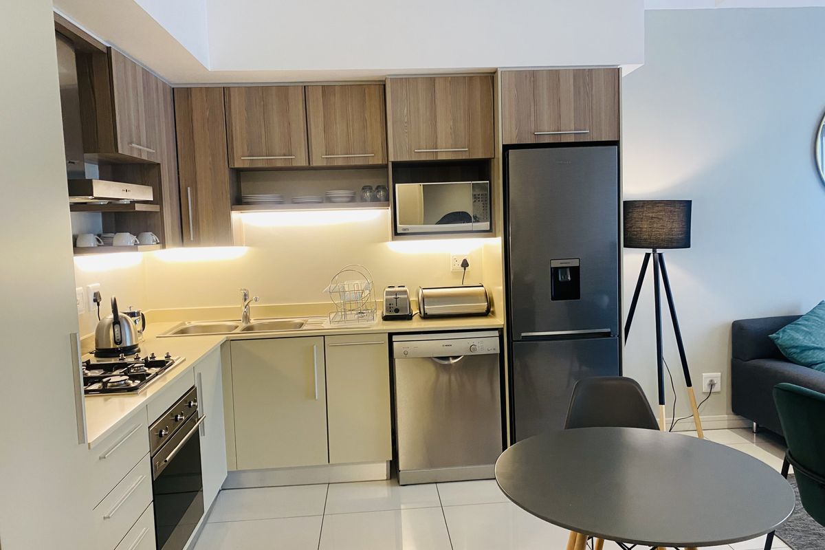 Modern kitchen featuring wood-finish cabinetry, integrated appliances, gas hob, built-in oven, and sleek tiled flooring with ambient under-cabinet lighting.