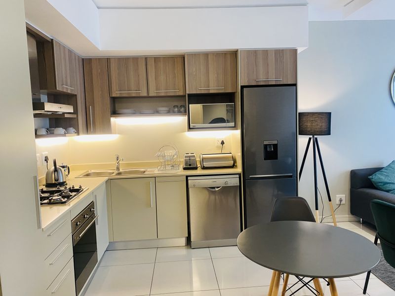 Modern kitchen featuring wood-finish cabinetry, integrated appliances, gas hob, built-in oven, and sleek tiled flooring with ambient under-cabinet lighting.