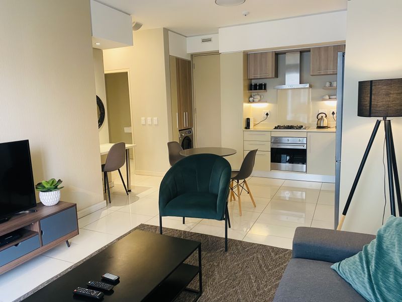 Modern open-plan living area featuring a compact kitchen with built-in appliances, sleek tiled flooring, and neutral finishes throughout.
