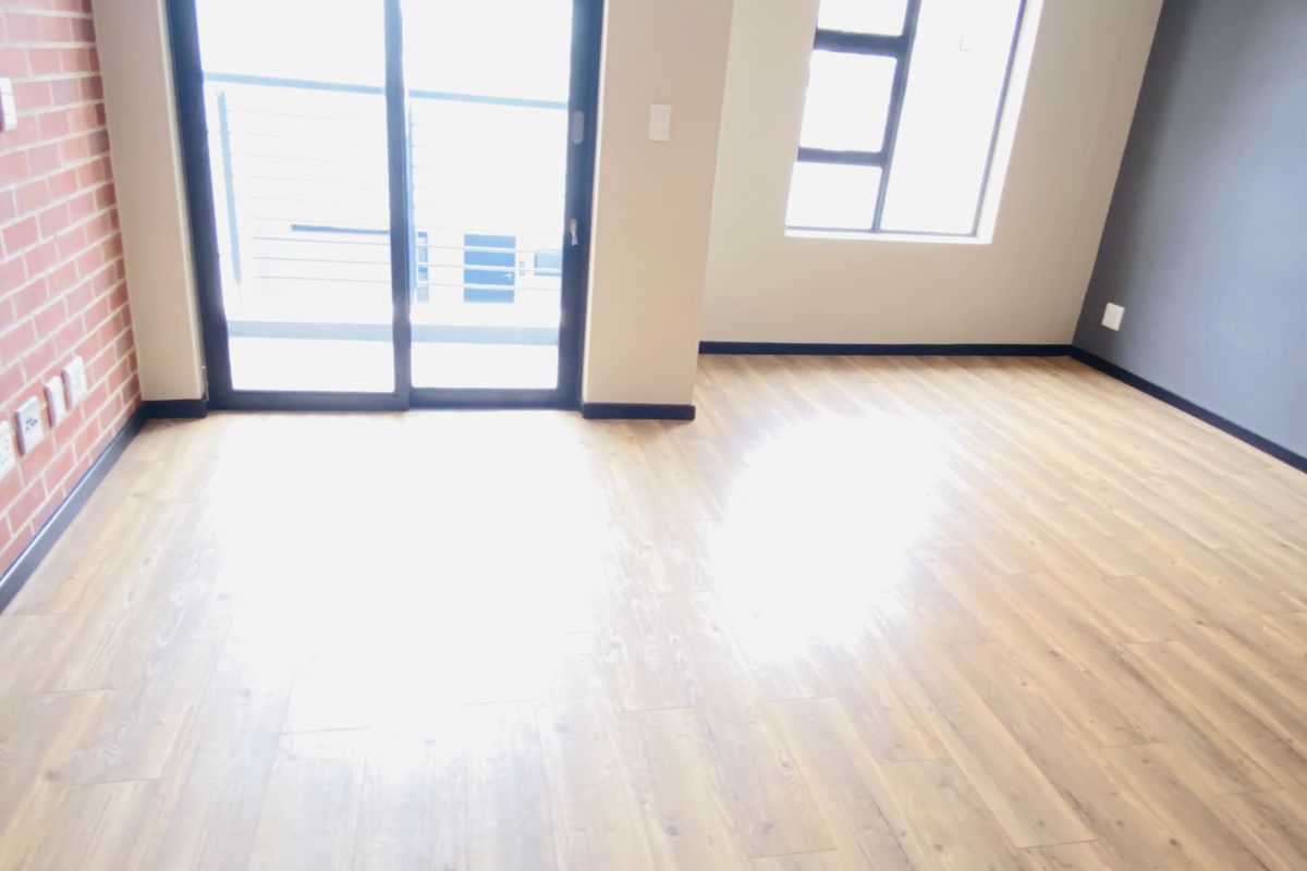 Bright and spacious living area featuring modern laminate flooring, an exposed brick accent wall, and large sliding doors leading to an outdoor space.
