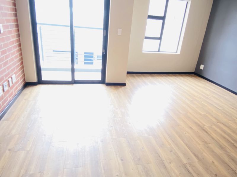 Bright and spacious living area featuring modern laminate flooring, an exposed brick accent wall, and large sliding doors leading to an outdoor space.