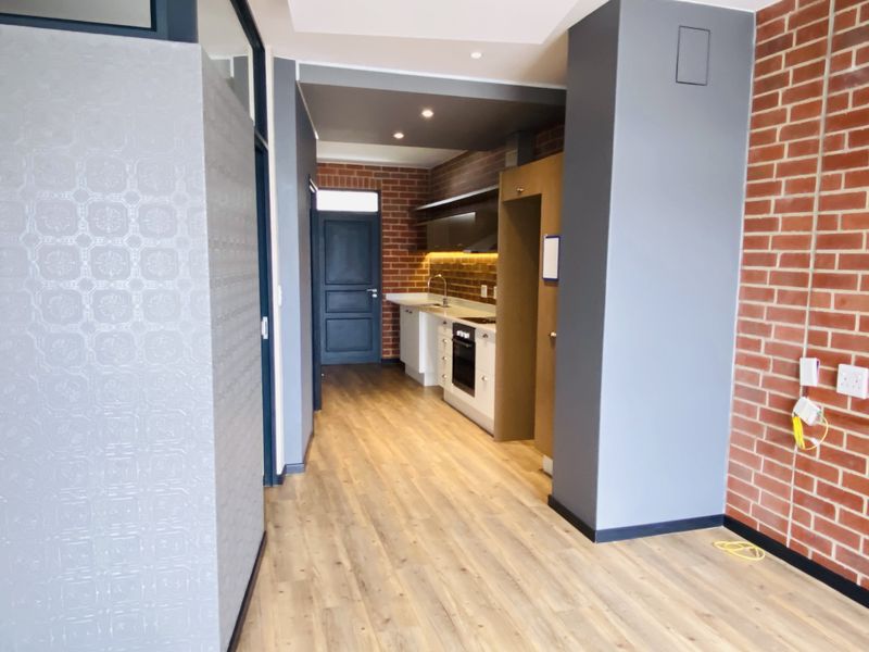 Modern kitchen area featuring sleek cabinetry, built-in appliances, laminate flooring, and an exposed brick feature wall in a contemporary open-plan layout.