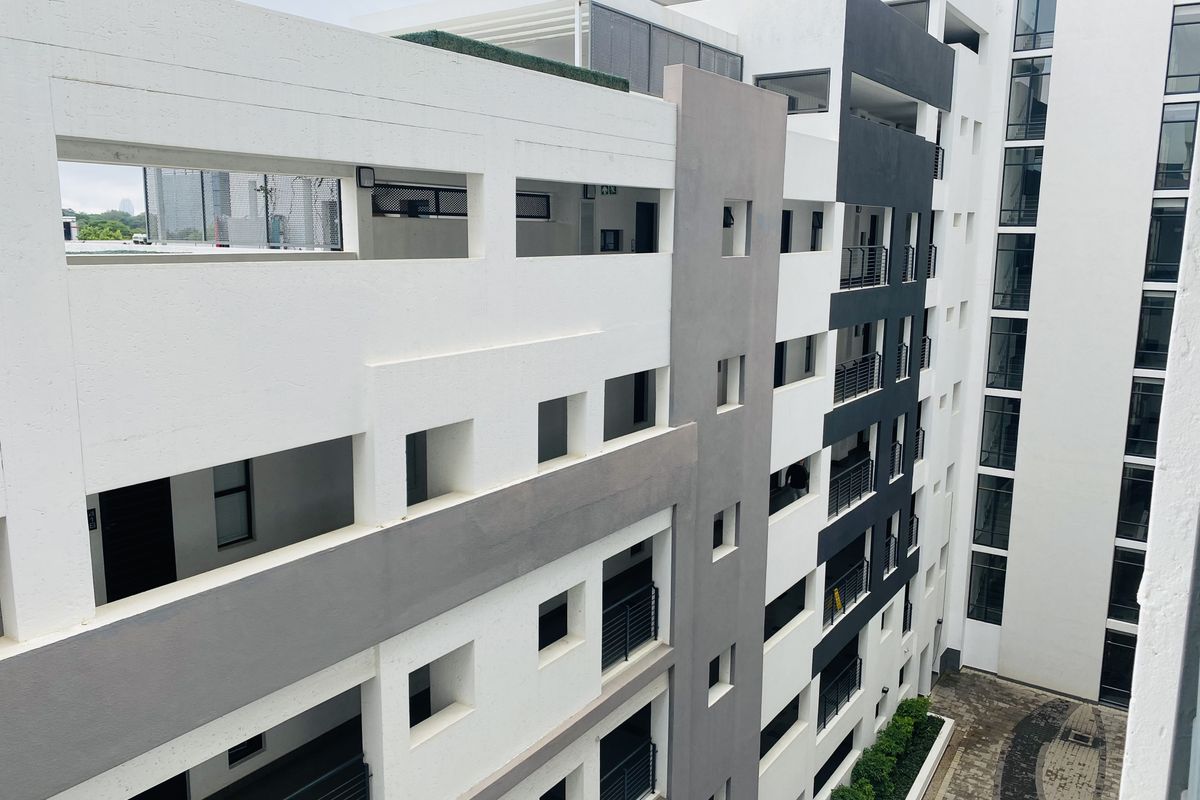 An elevated view of the apartment building exterior, showcasing modern architectural design, private balconies, and a paved ground-level courtyard area.