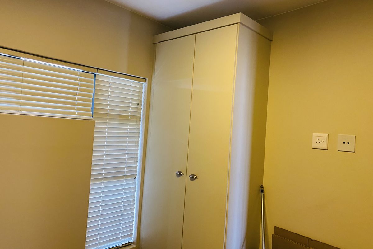 A clean bedroom featuring a tall built-in wardrobe and venetian blinds, providing a neutral and functional space ready for personalization.