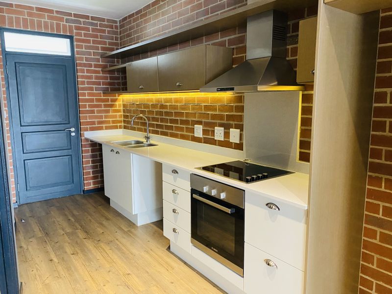 Modern kitchen featuring white cabinetry, stone countertops, integrated stainless steel appliances, and a stylish exposed brick feature wall with under-cabinet lighting.