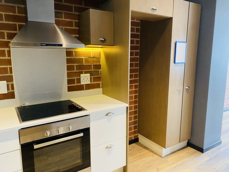 Modern kitchen featuring exposed brick accents, stone countertops, built-in oven, electric hob, and integrated cabinetry with ample storage space.