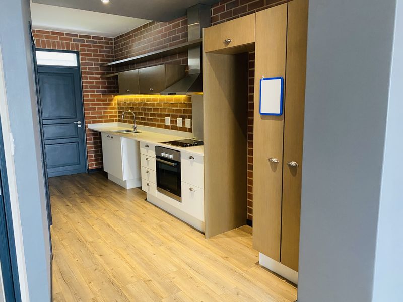 Modern kitchen featuring exposed brick walls, sleek white cabinetry, integrated appliances, and warm wood-look flooring with efficient under-cabinet lighting.