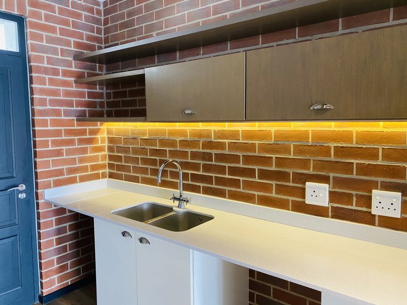 Modern kitchen area featuring exposed brick walls, quartz countertops, stainless steel double sink, and integrated under-cabinet LED lighting.