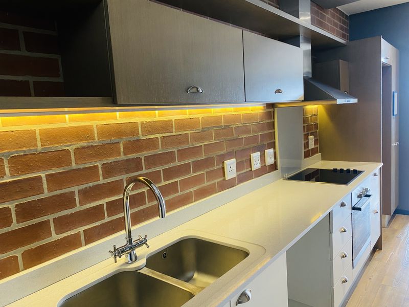 Modern kitchen featuring sleek cabinetry, stone countertops, integrated appliances, and a stylish brick splashback with ambient under-cabinet lighting.