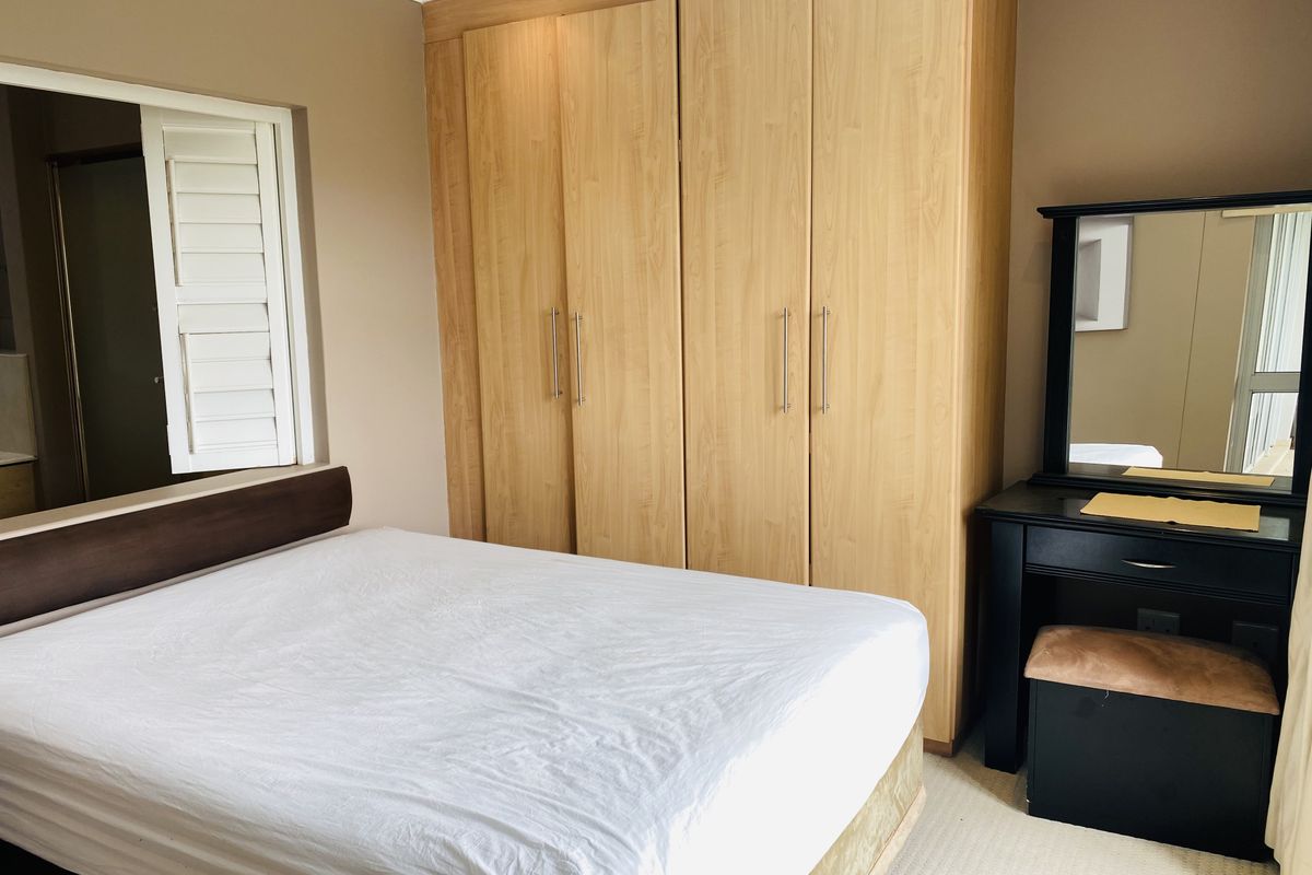 A bedroom featuring built-in wooden cabinetry and a window with plantation-style shutters, offering a functional and neutral living space.