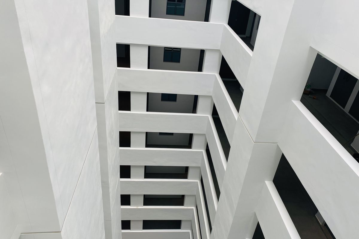 A vertical view looking down an open-air apartment building atrium featuring white structural walls and multiple levels of balcony walkways.
