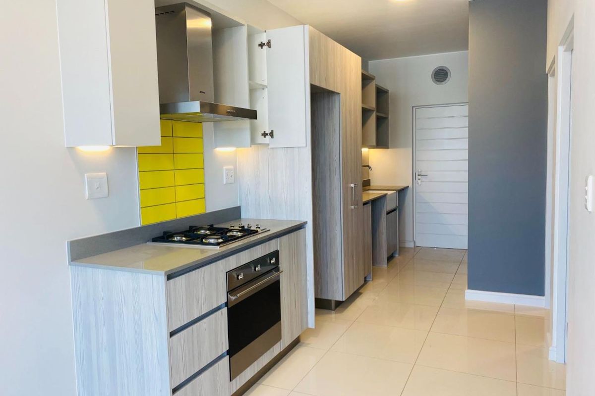 Modern kitchen featuring light wood-grain cabinetry, stone countertops, a gas hob, built-in oven, and a vibrant yellow tiled splashback.