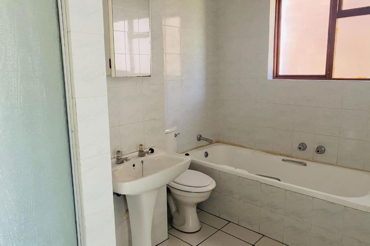 A functional bathroom featuring a pedestal basin, toilet, and a built-in bathtub with tiled walls and flooring.