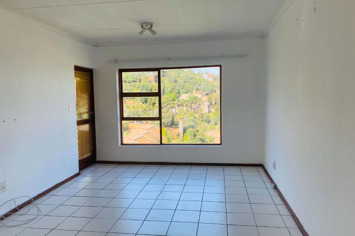 A bright, empty living area featuring tiled flooring, a large window with scenic views, and a glass-paneled door leading to an outdoor space.